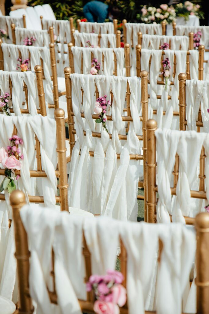 Rows of outdoor wedding chairs adorned with white drapery and pink flowers.