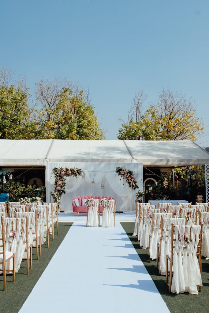 Elegant outdoor wedding setup with decorated chairs and floral arrangements under a clear blue sky.